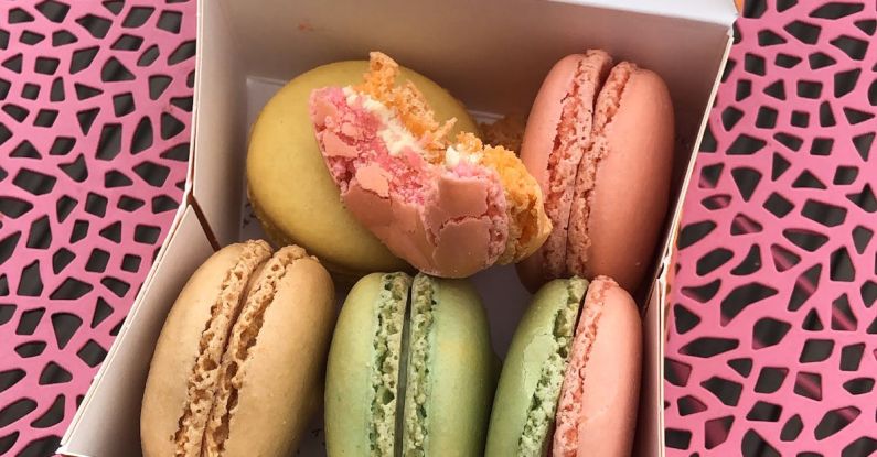 Dessert Spots - From above of cardboard container filled with delicious colorful macaroons placed on pink surface with black details