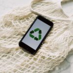 Sustainable Viewing - Overhead of smartphone with simple recycling sign on screen placed on white eco friendly mesh bag on marble table in room
